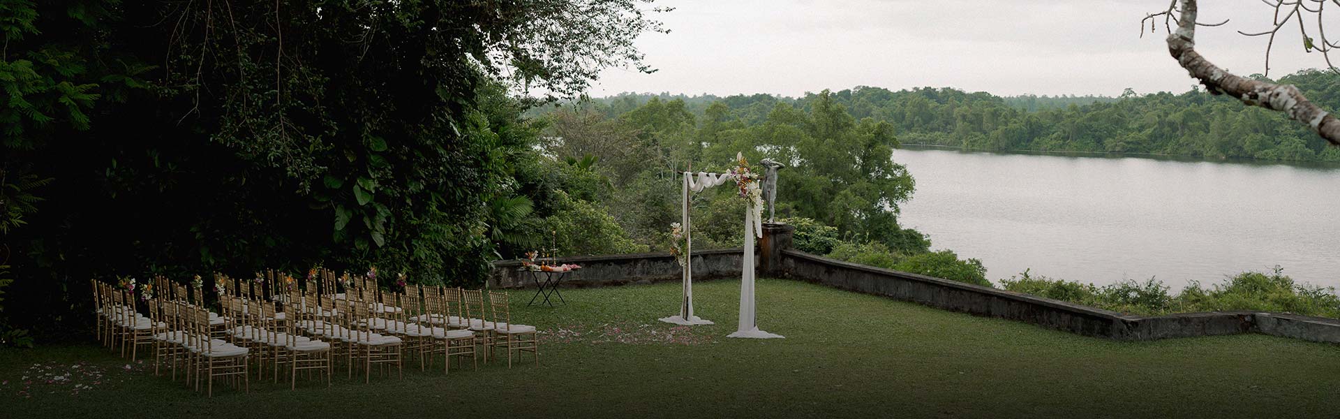 A luxury garden wedding hotel in Bentota at Lunuganga, featuring a floral arch, golden chairs, and a lakeside view.