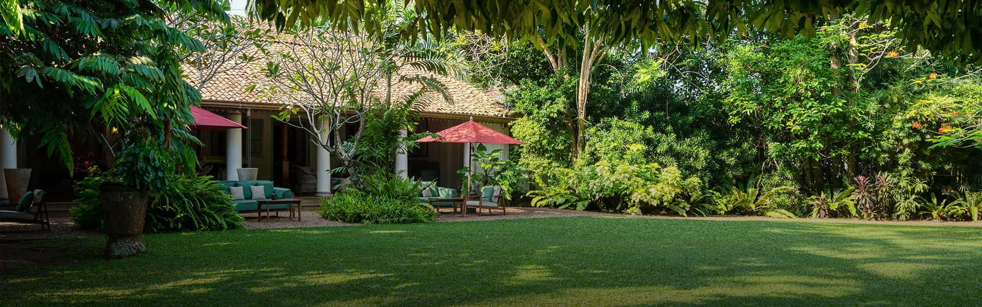 Teardrop luxury hotel in Sri Lanka, featuring a lush green garden with seating area and a traditional bungalow surrounded by nature.