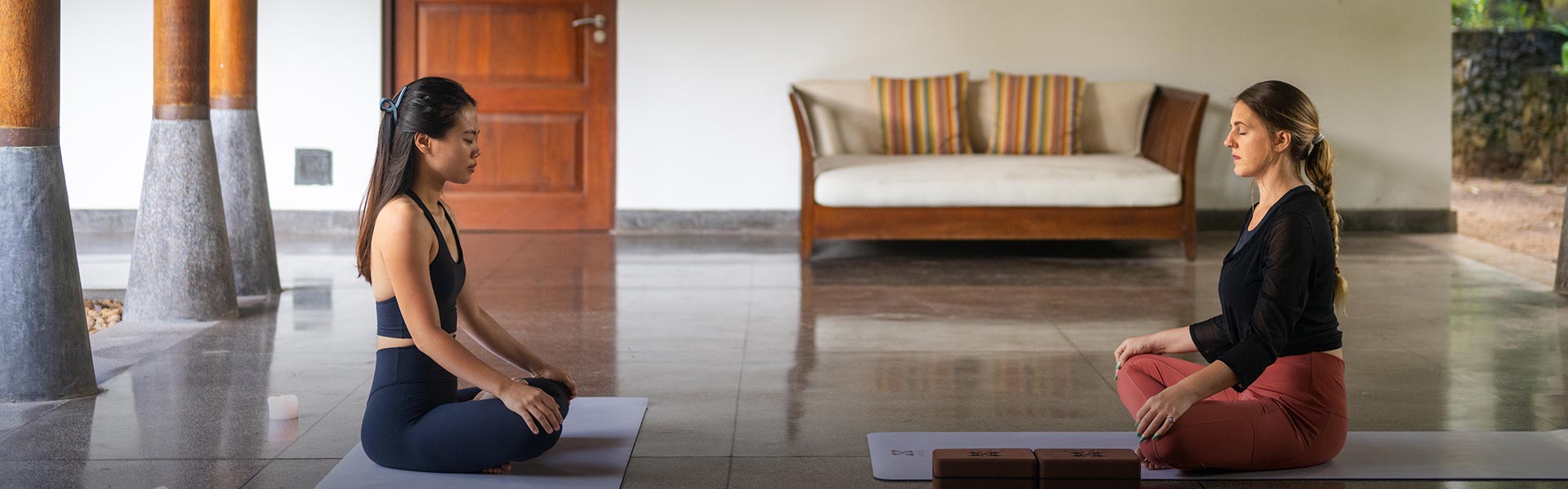 Two women meditating on yoga mats in a minimalist hotel room, experiencing Teardrop Hotels' luxury wellness packages in Sri Lanka.